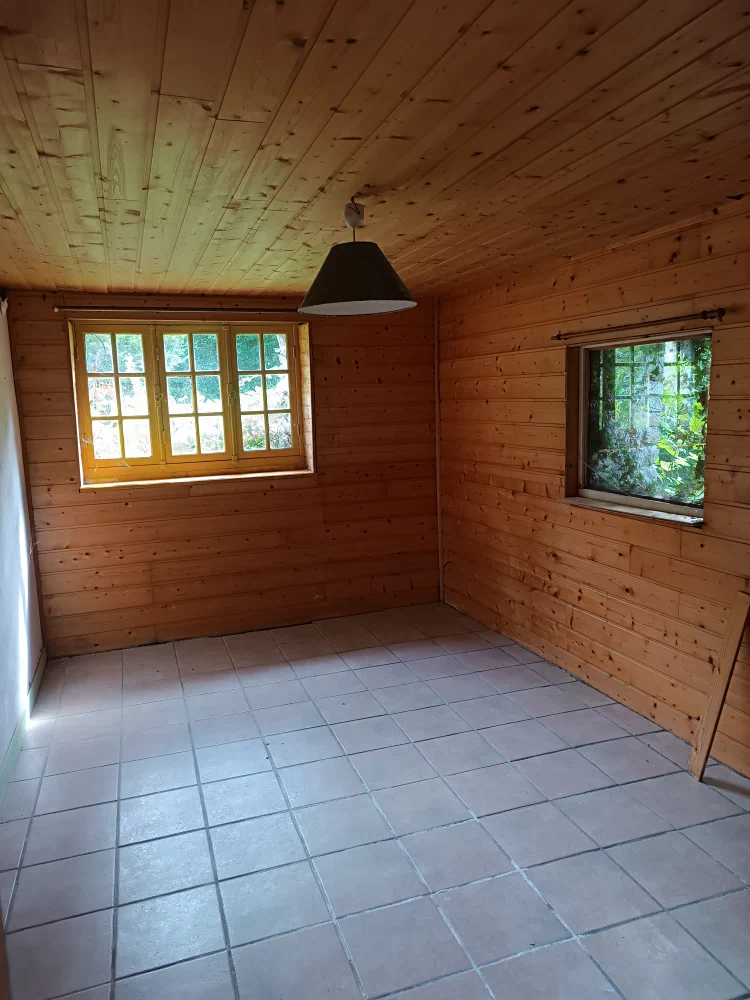 Une chambre entièrement lambrissée de bois clair, éclairée par deux fenêtres donnant sur la verdure