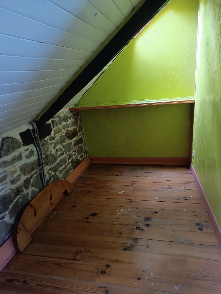Un espace sous rampant aux murs vert anis, avec son parquet en bois et son mur de pierre apparente